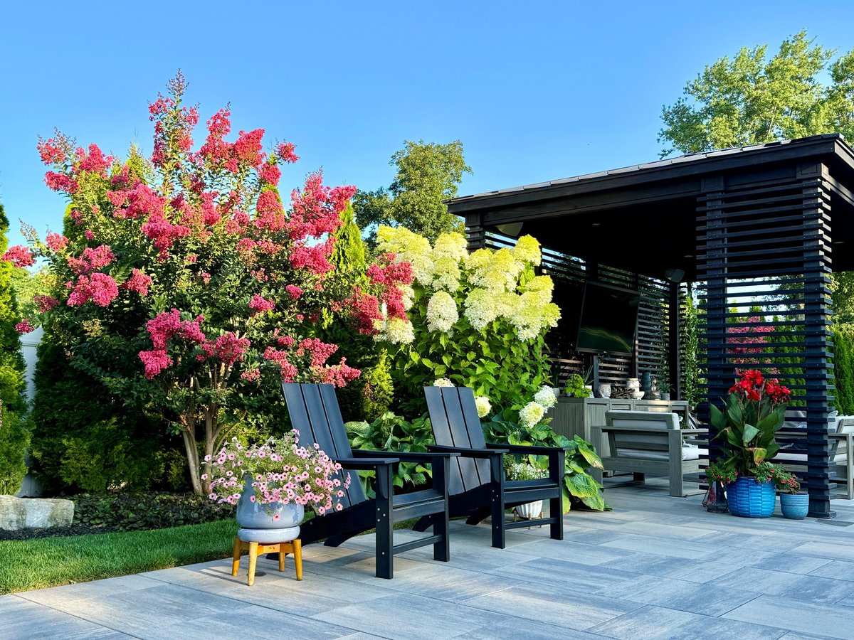 Lush, upscale backyard landscape with colorful perennials, shrubs, stylish gray pavers, and comfortable seating around a fire feature.
