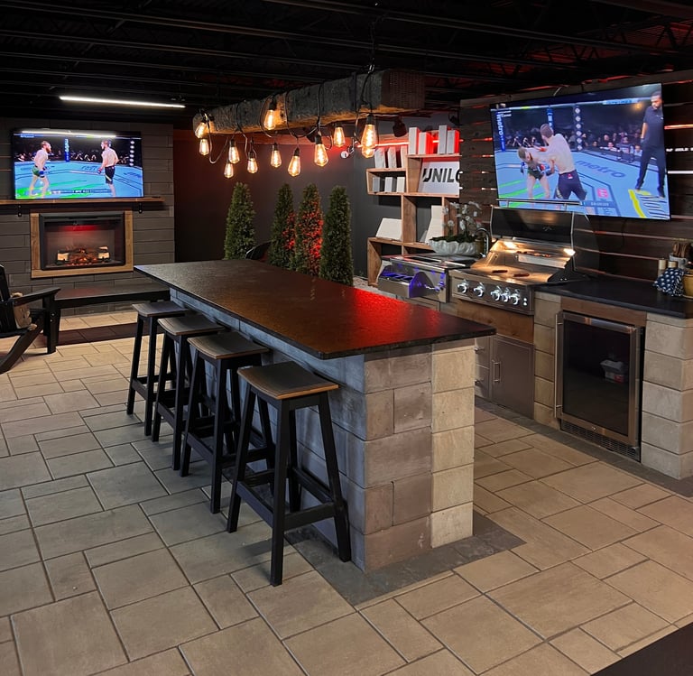 Modern basement entertainment space with large island counter, bar seating, TVs, fireplace, and pendant lighting