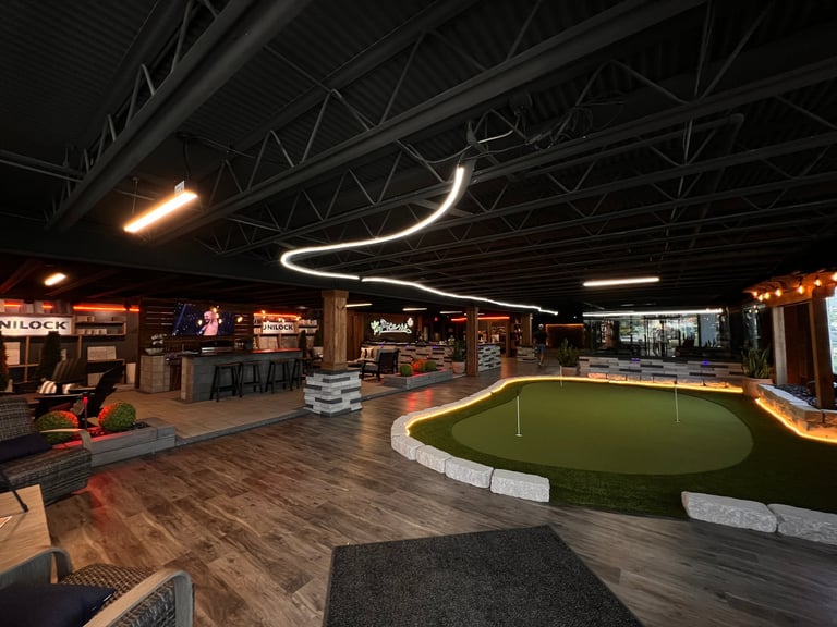 Modern indoor mini golf facility with illuminated neon ceiling lights and wooden flooring at night