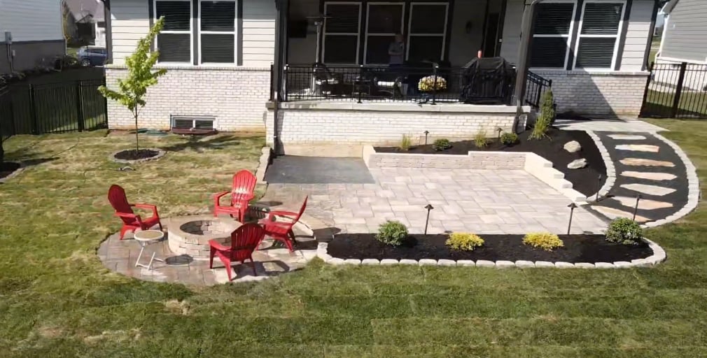 Backyard patio with red Adirondack chairs, fire pit, and curved landscaping beds next to a brick house